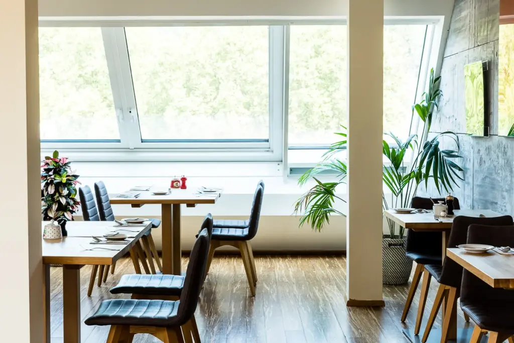 heller Raum mit großem Schraegfenster, grauen Stühlen und Eichentischen