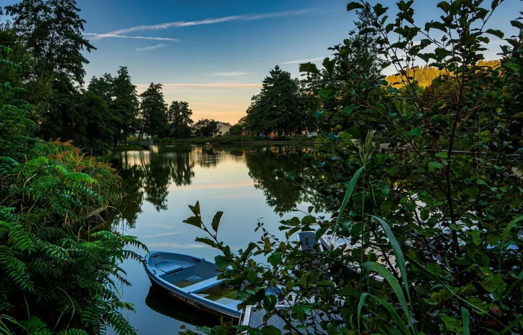 kleiner Stadtsee umrandet mit vielen gruenen Baeumen und Bueschen bei Sonnenuntergang