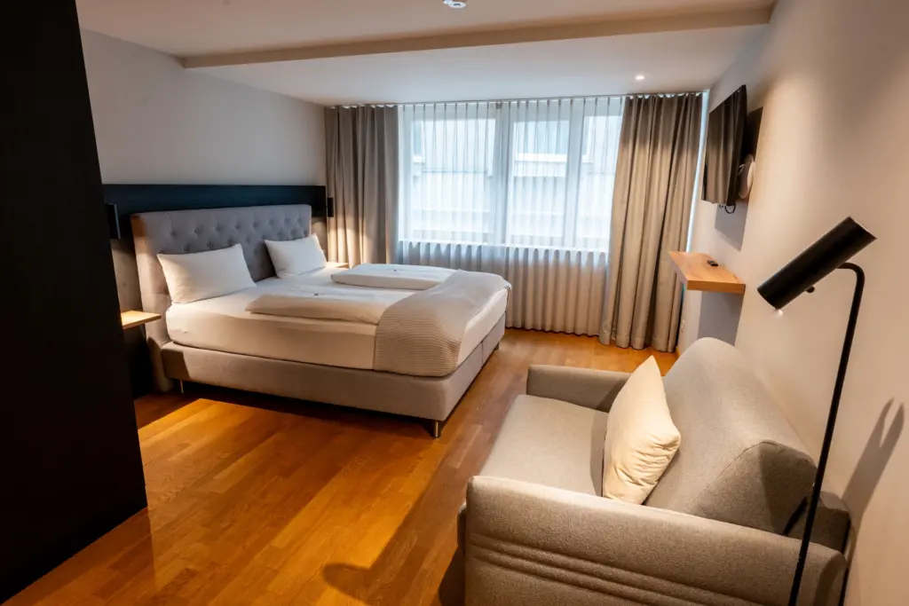 Schlafraum mit Eichenparkett, schwarzem Schrank, Boxspringbett, Sessel und Stehlampe