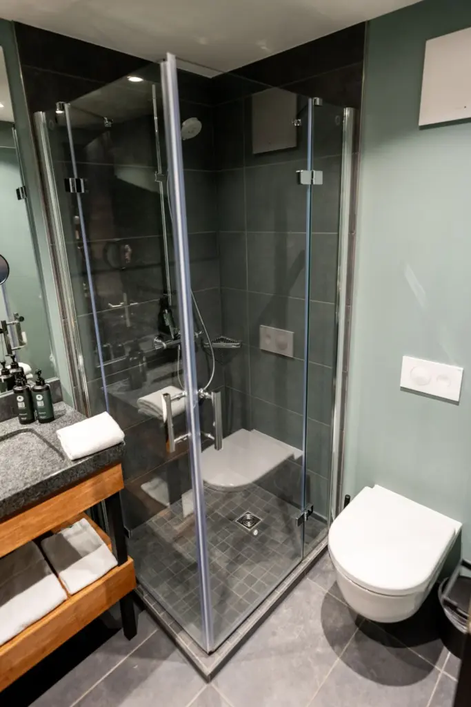 dunkelgrau gefliestes Badezimmer mit Eckdusche aus Glas, Granitwaschbecken und Holzwaschtisch