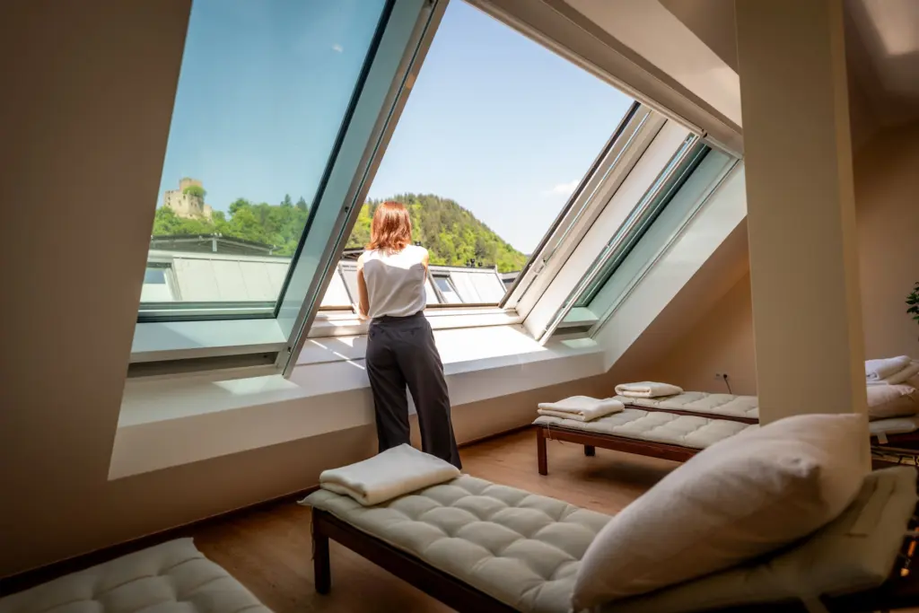heller Raum mit Liegen, geoeffnetem Schraegfenster und Blick zur Kastelburg