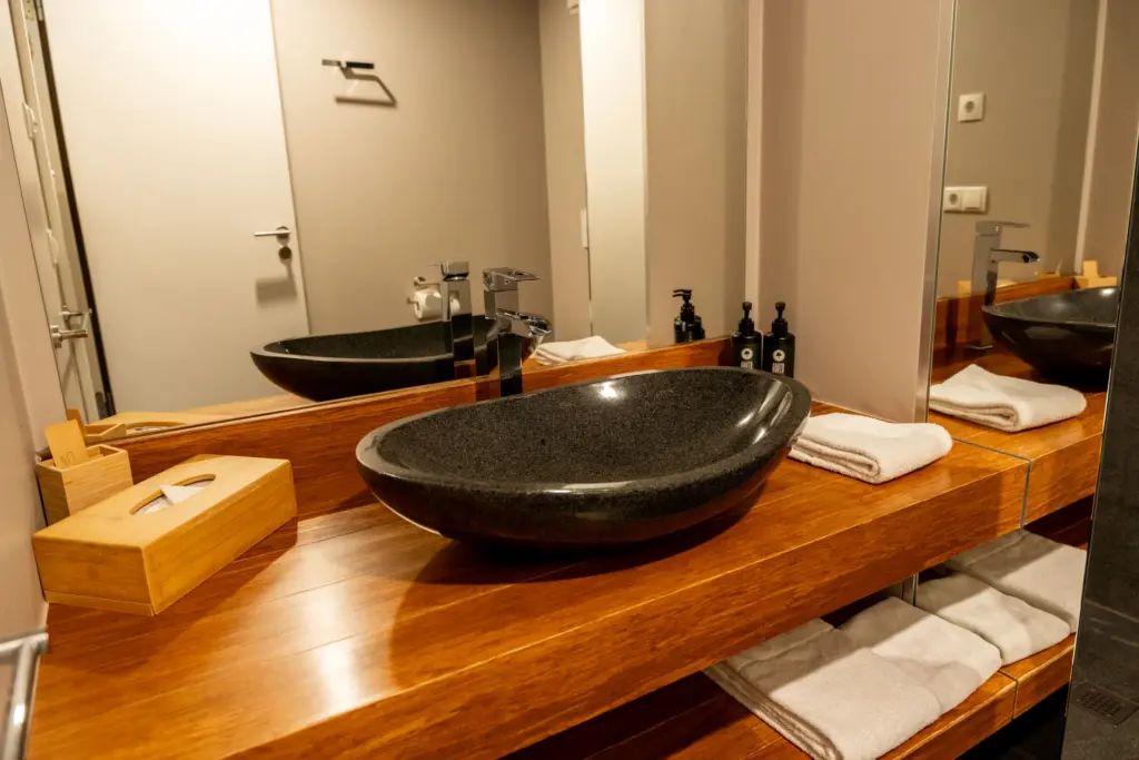 großzuegiger Holzwaschtisch mit Granitwaschbecken, flauschigen Handtuechern und Hotelkosmetik