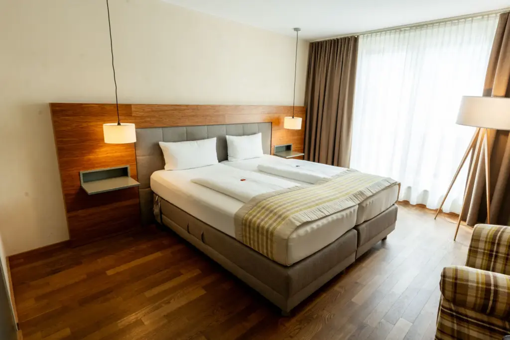 warm eingerichtetes, großzuegiges Hotelzimmer mit Boxspringbett, Sessel und Stehlampe