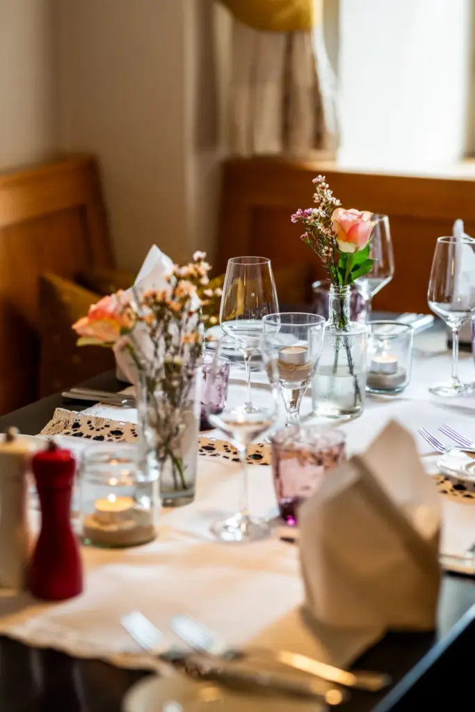 eingedeckter Tisch mit Spitzen Tischdecke, Besteck, Brottellern, Stoffservietten, frischen Blumen und Kerzen
