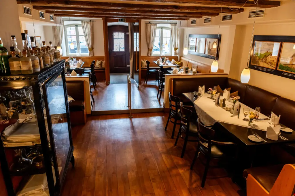 Blick in unser Restaurant mit warmen Hölzern, fein eingedeckten Tischen und unserem Spirituosen und Wäscheschrank
