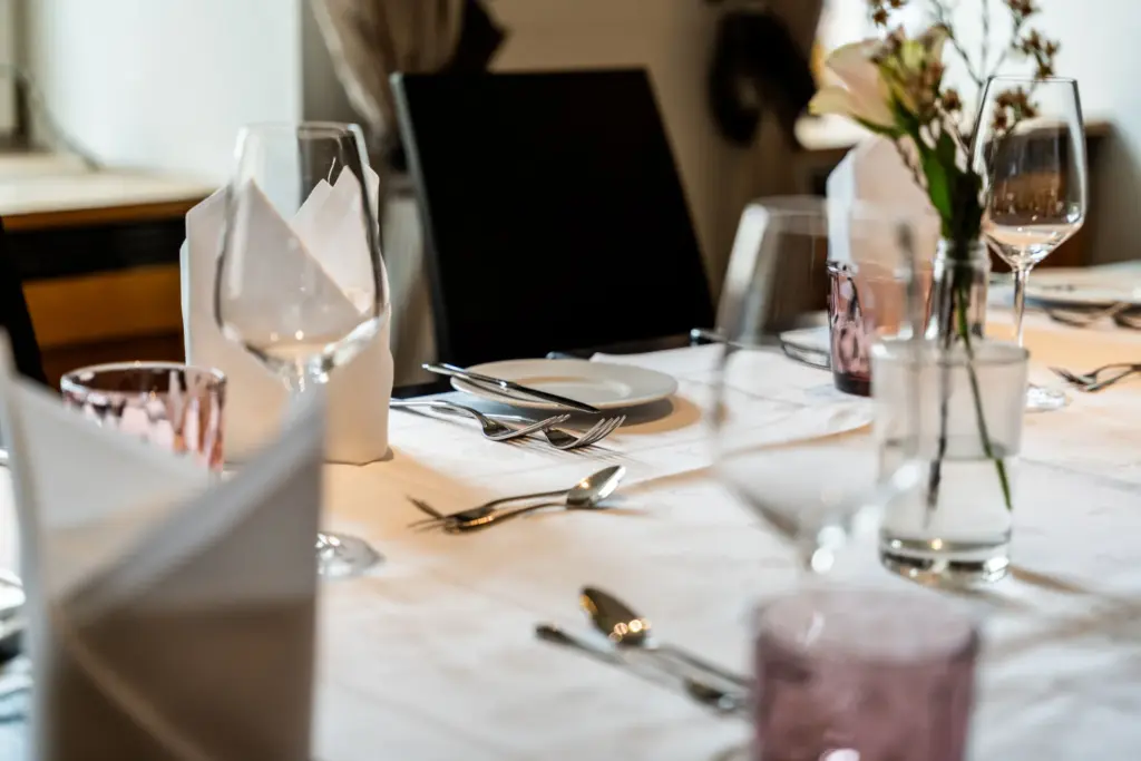 Detailaufnahme einer großen, gedeckten Tafel mit weißer Tischdecke, Stoffservietten, und frischen Blumen