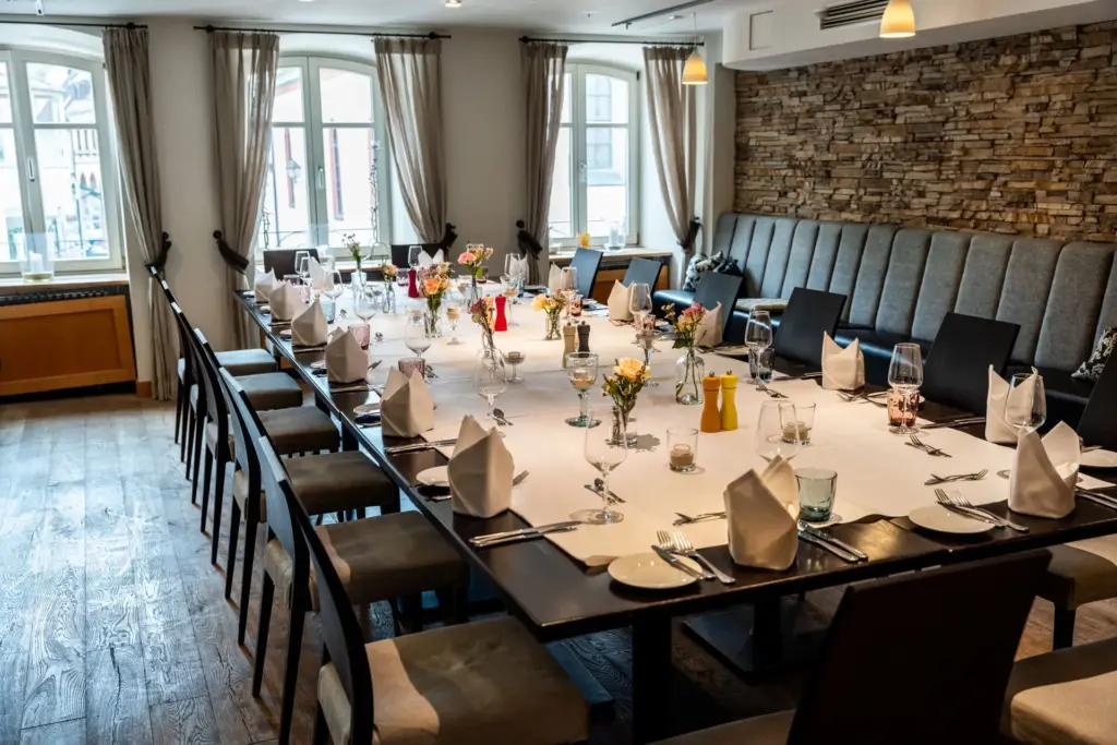 große, festlich gedeckte Tafel in unserem Veranstaltungsraum mit Holzparkett und Bruchsteinwand
